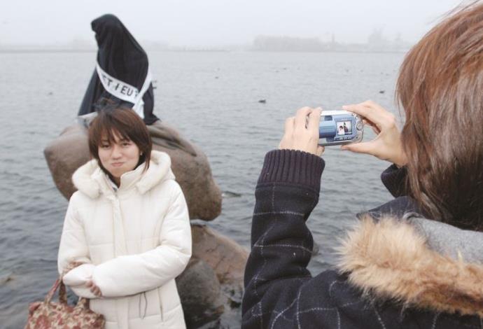 תיירות מצטלמות בקופנהאגן על רקע פסל בת הים הקטנה שכוסה בבורקה (צילום:  רויטרס)
