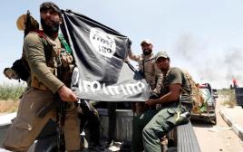 לוחמים שיעים מציגים דגל דאעש שנתפס בלחימה בפלוג'ה (צילום: רויטרס)