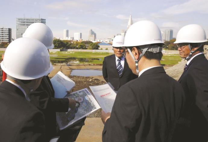 מהנדסים יפנים על הרקע השטח בו יקום האצטדיון האולימפי (צילום:  רויטרס)